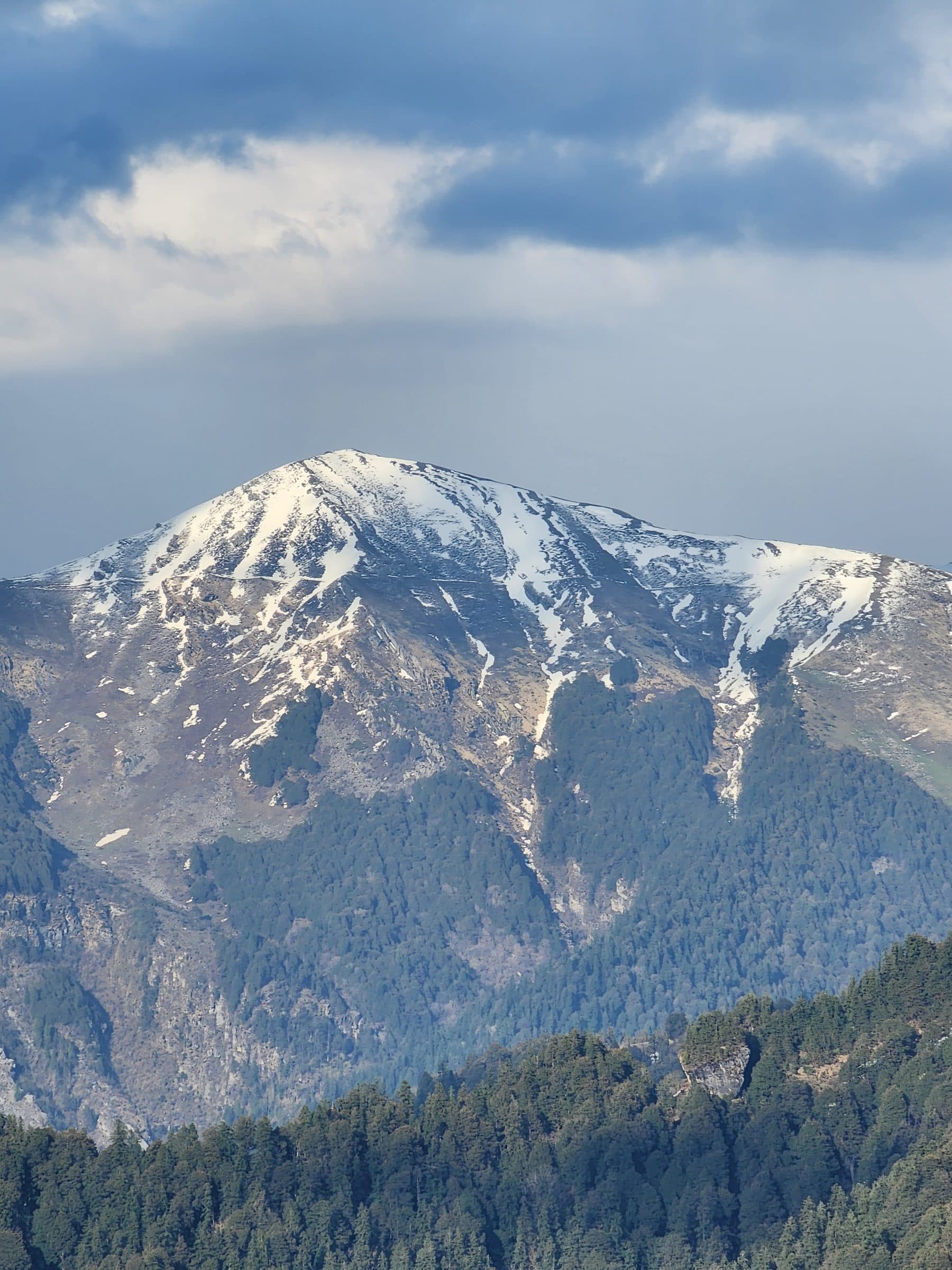 Panoramic view of forested mountains with snow patches under a cloudy sky