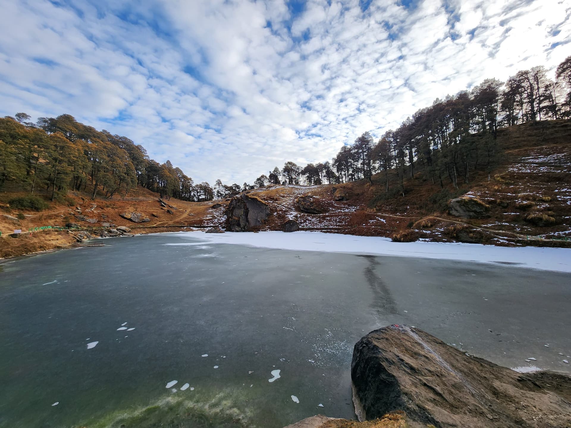 A cold body of water surrounded by grassy slopes and trees under a blue sky