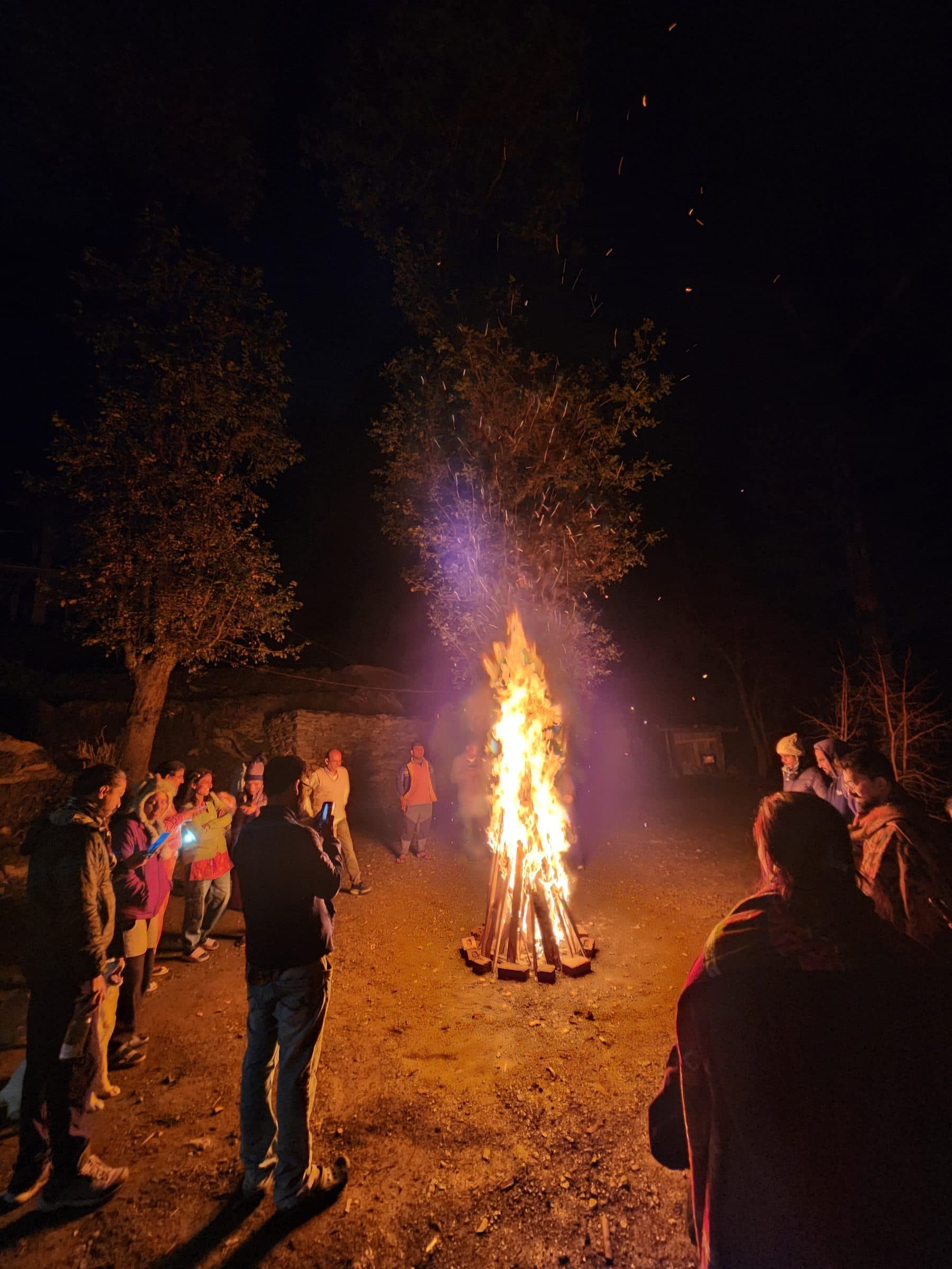 Group of people standing near a large bonfire in a wooded area