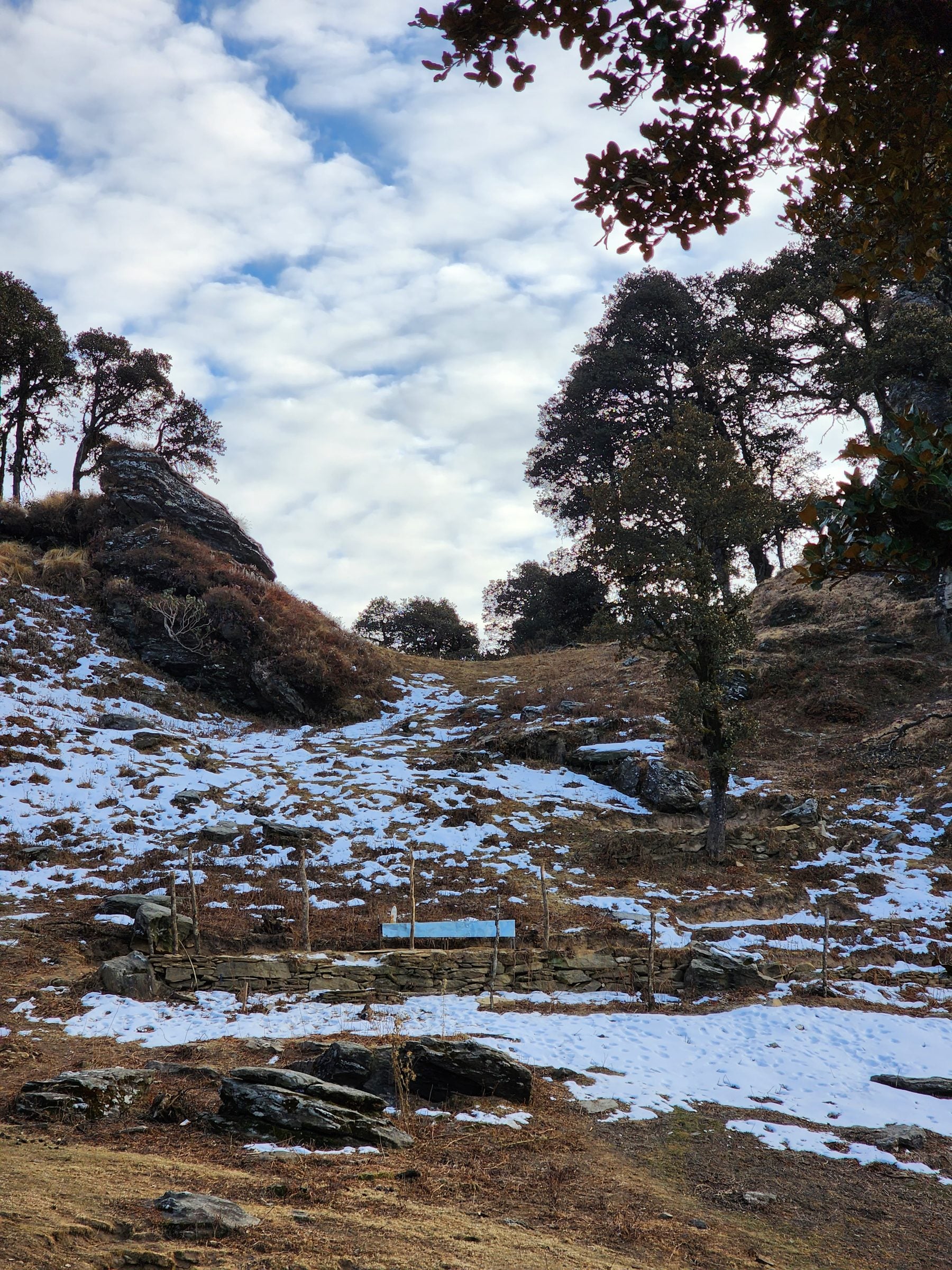 A serene, snow-dusted hillside in Jibhi Valley, Himachal Pradesh, with wooden signs and autumn grasses.
