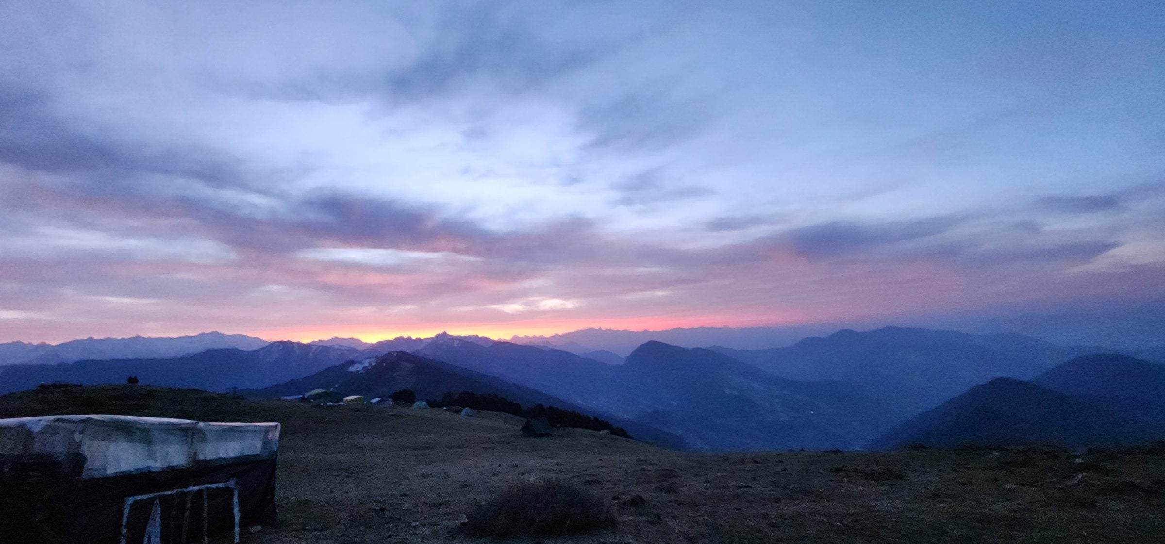 A stunning panoramic view of Shoja village, Himachal Pradesh, India at dusk with a rocky hillside and a stone wall.