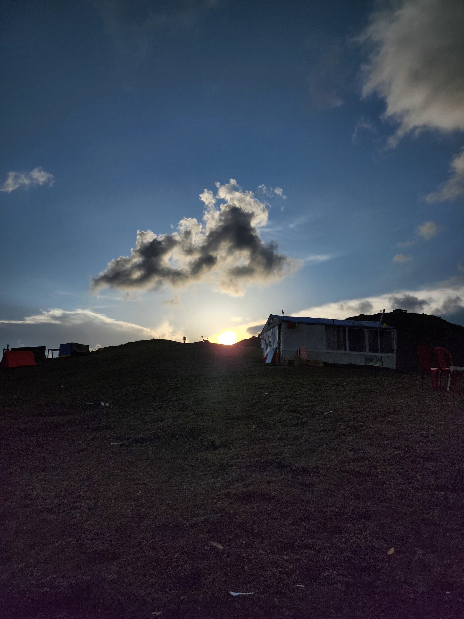 A solitary wooden bench sits under a partially cloudy sky in the picturesque Shoja Valley, Himachal Pradesh, India.