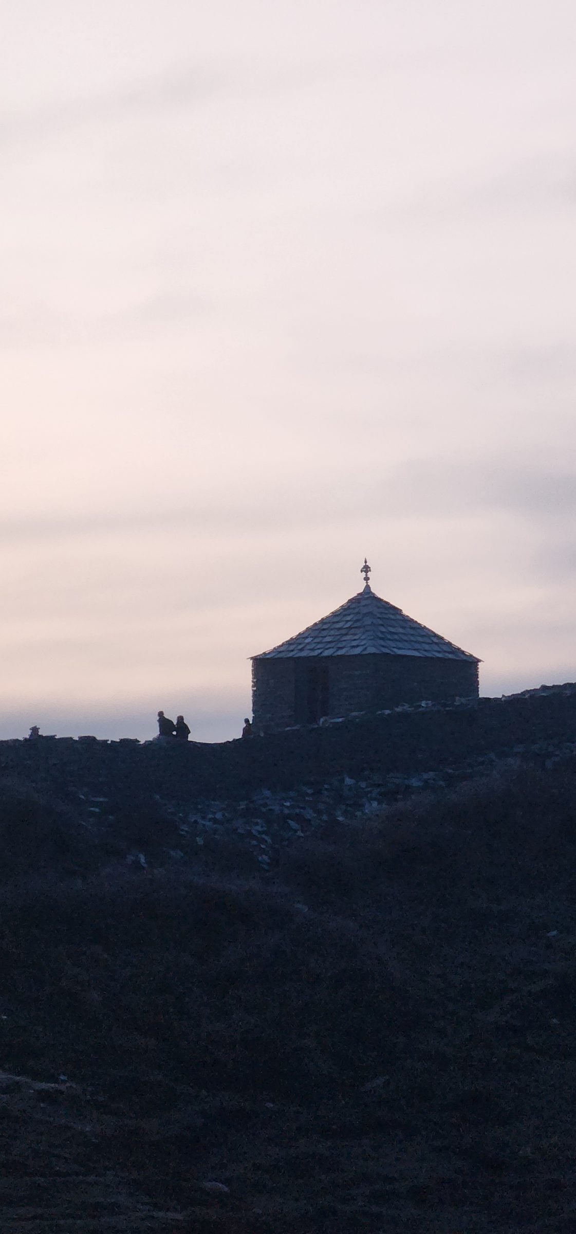 A solitary stone structure sits in the dark valley of Jibhi, Himachal Pradesh, India, under a vast evening sky.