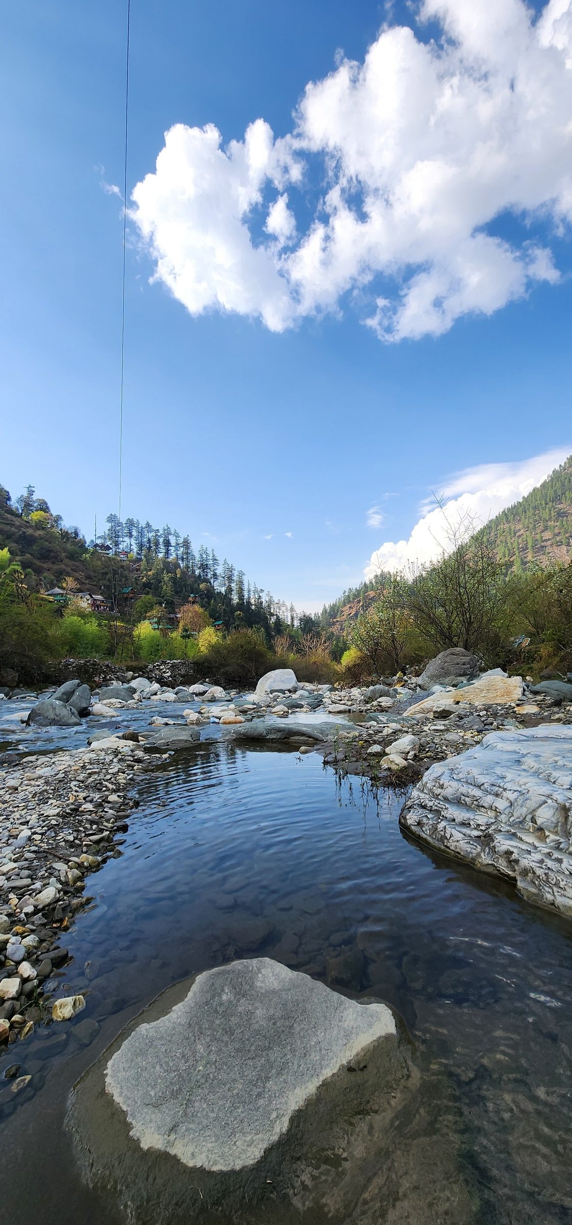 A wide shallow reach of the Tirthan river near Jibhi, smooth boulders and clear pools under a blue sky