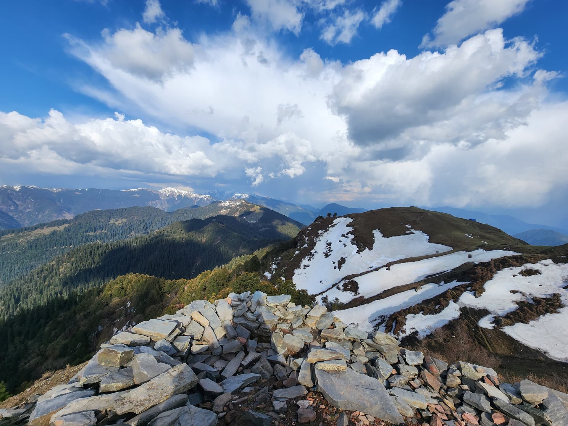 Snow-covered peaks and a tranquil valley landscape in Jibhi Valley, Himachal Pradesh, India.